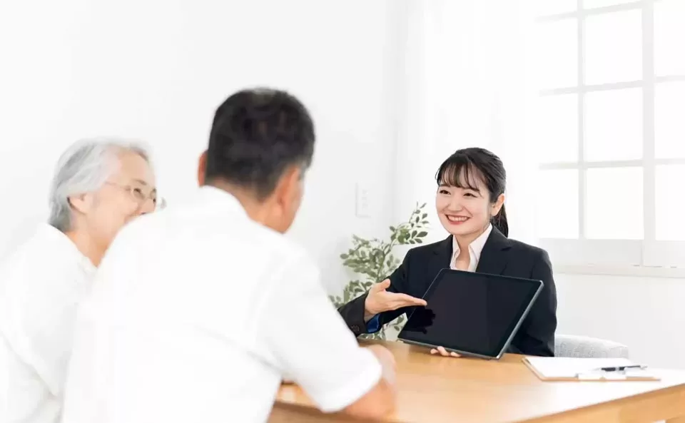 葛飾区メモリーホーム新小岩の女性スタッフがタブレットを見せながら高齢の男女に相談を行っている場面